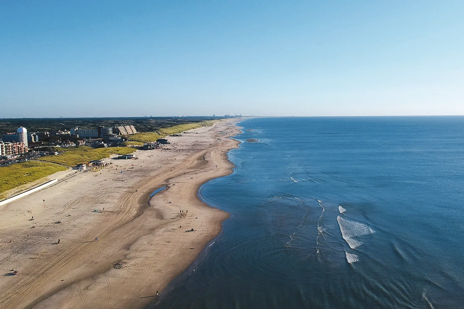 Foto aérea da praia de areia perto de Egmond aan Zee, com poucas pessoas e o mar ao fundo, sob um céu limpo