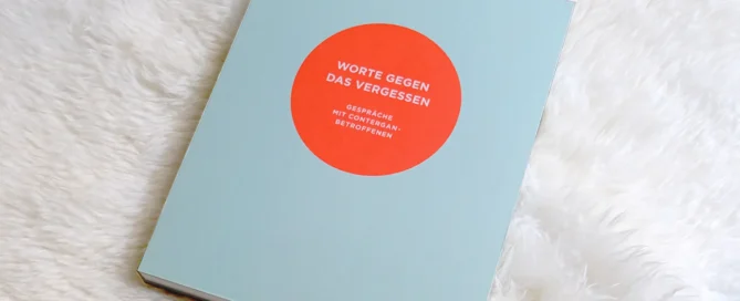 Ein türkises Buch mit Schrift in einem Neon-Orangefarbenen Kreis liegt auf einem künstlichen Lammfell